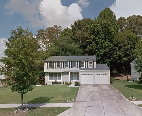 White two-story assisted living facility with driveway, garage, and manicured lawn.
