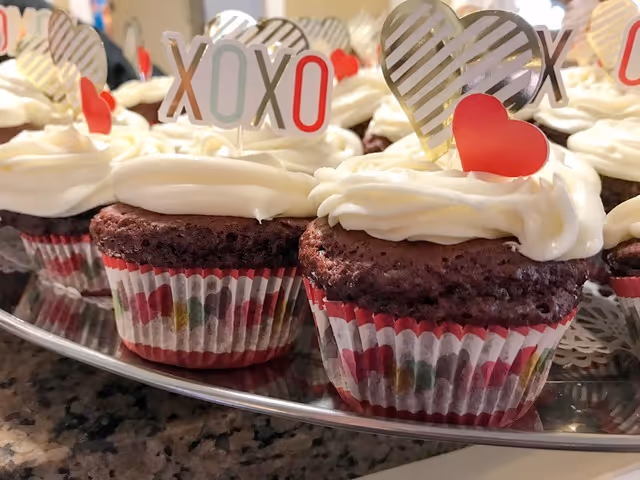Plate of frosted cupcakes decorated with XOXO and heart toppers on a countertop.