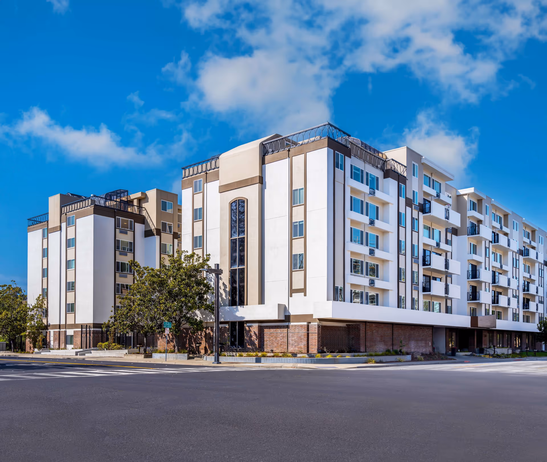 Exterior view of a multi-story modern apartment building with balconies and trees under a blue sky.