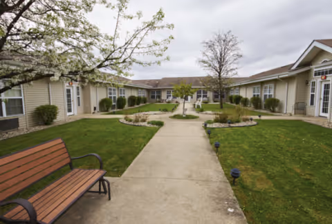 Courtyard with a central concrete path, benches, manicured lawns, and single-story facility buildings surrounding it.