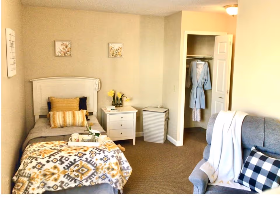 Cozy bedroom with a single bed, nightstand, closet, and small seating area.