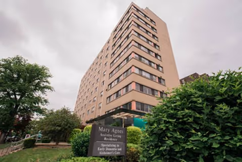 Tall beige senior living building with landscaping in the foreground and a Mary Agnes Manor sign