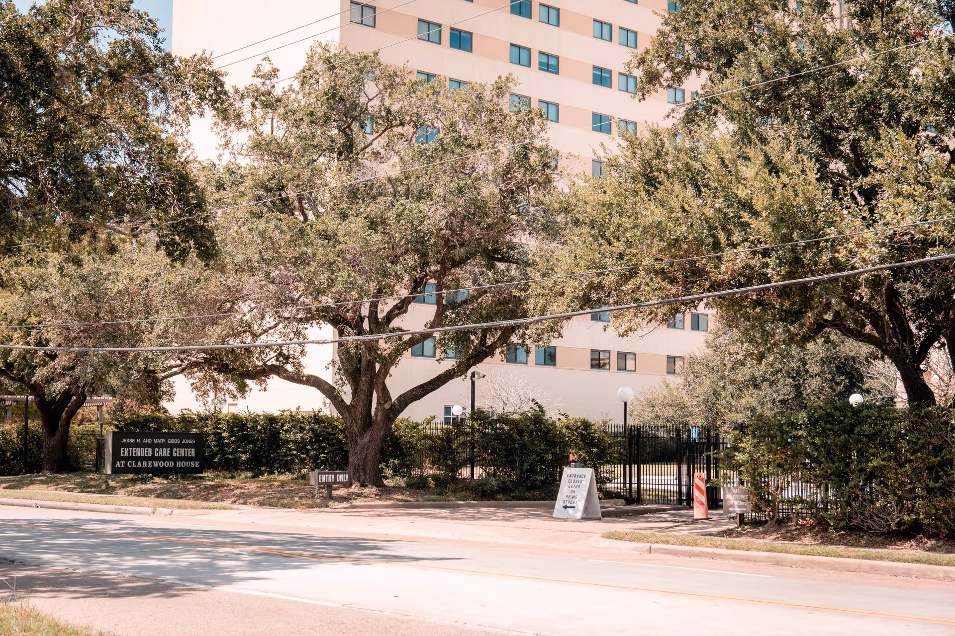 Front view of the Clarewood House extended care center building behind trees with a gated entrance and signage.