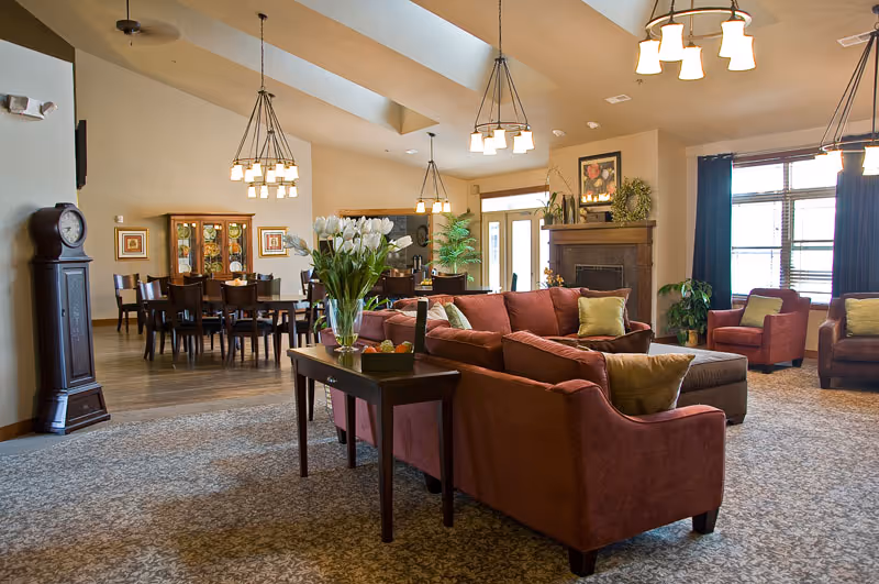 Spacious senior living lobby with red sofas, tables, plants, and a fireplace.