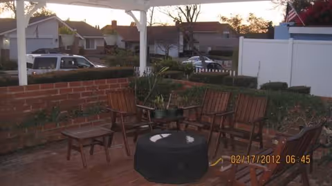 Outdoor seating area with wooden chairs around a central fire pit under a white pergola.