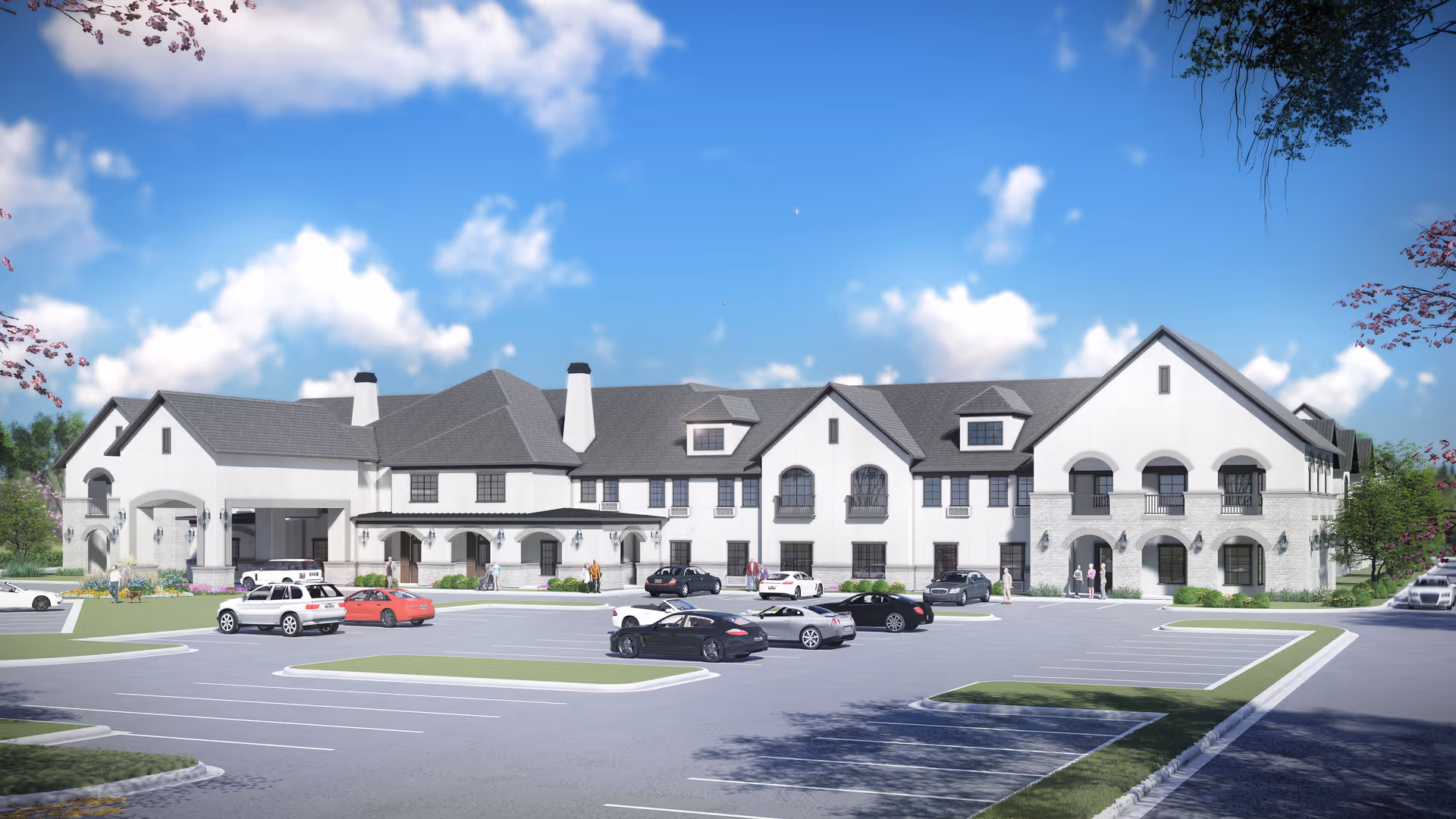 Exterior view of a large, two-story senior living facility building with white walls and gray roofing under a blue sky with scattered clouds. Several cars are parked in the parking lot in front of the building, and a few people are walking near the entrance. Trees with pink blossoms frame the image on the sides.
