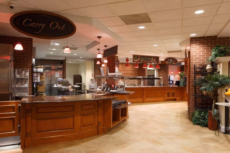 Empty cafeteria-style serving area with wooden service counters, hanging red lights, and a 'Carry Out' sign.