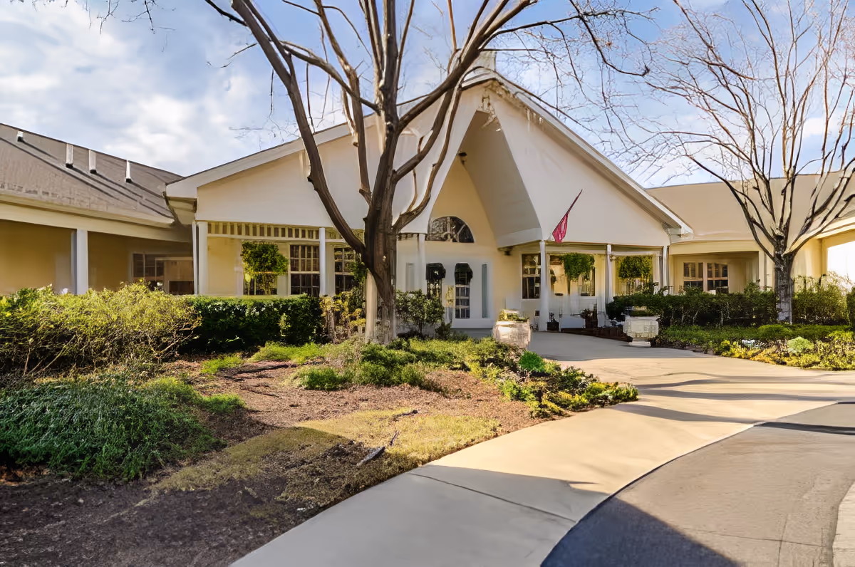 Front exterior view of TerraBella Southport facility showing a single-story building with a peaked roof, large windows, a covered entrance, and landscaped greenery including bushes and trees.