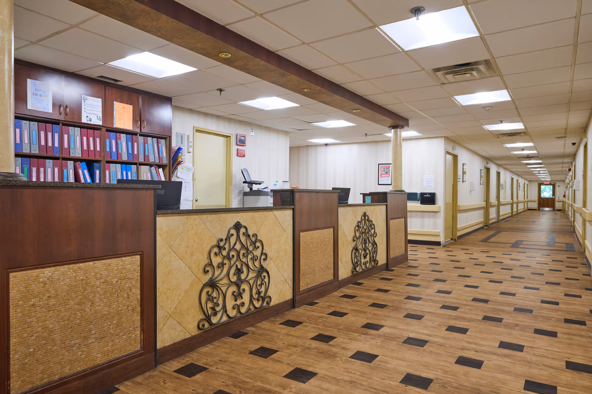 Reception desk and long interior hallway of a senior care facility with file shelves and decorative panels.