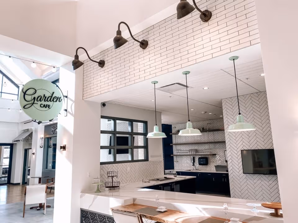 Bright modern indoor café with pendant lights, a service counter, and a 'Garden Cafe' sign.