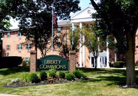 Exterior view of a brick senior living building with a green Liberty Commons sign near entrance.