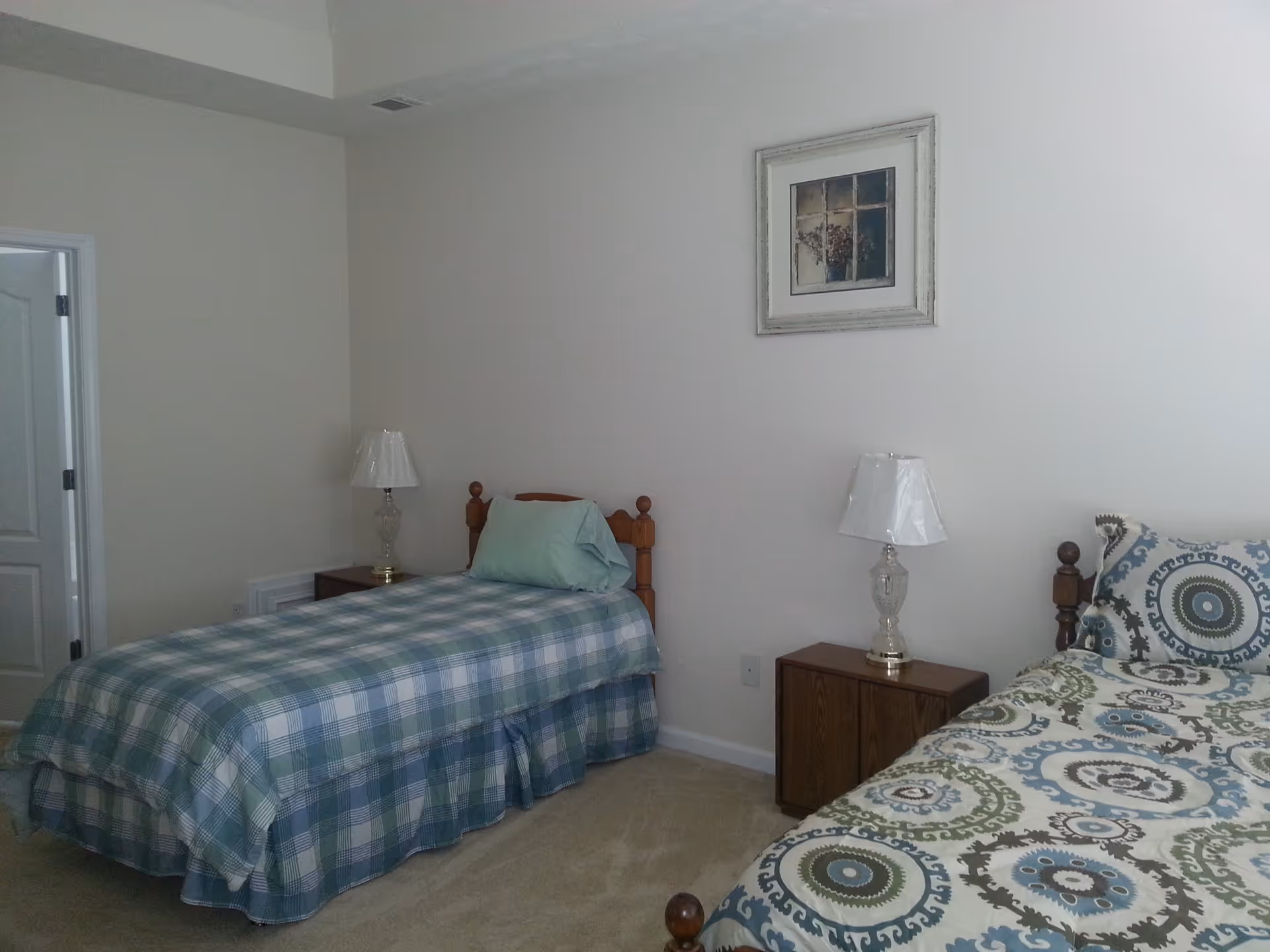 Simple bedroom with two twin beds, nightstands and lamps against a pale wall with framed art.