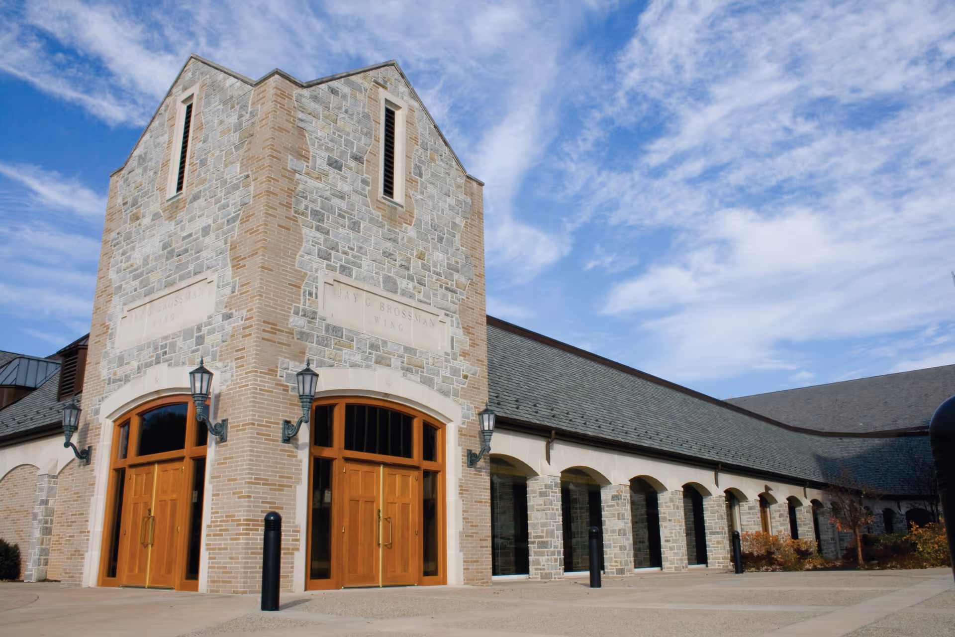 Stone and brick community building with a tower and arched wooden double doors under a blue sky.