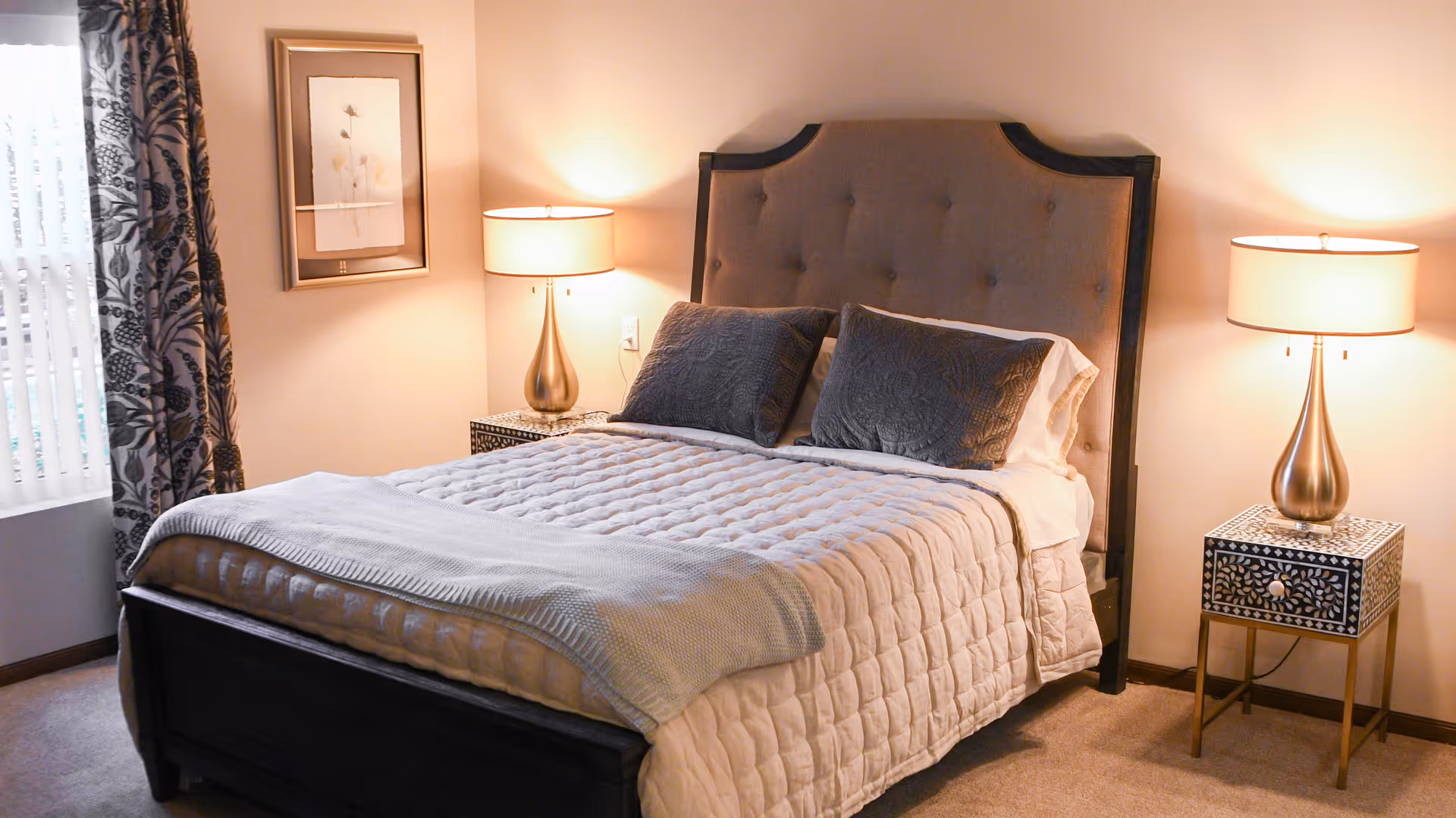 Neatly made bedroom featuring a tufted headboard bed flanked by patterned nightstands and matching lamps.
