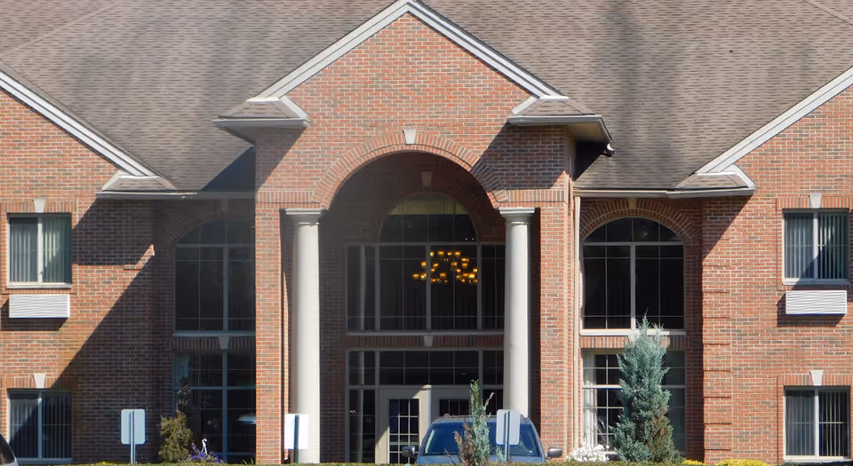 Brick building facade with an arched main entrance flanked by columns and large windows.