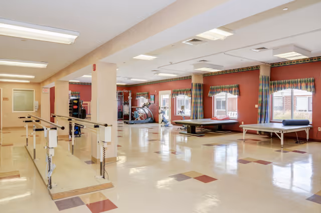 Spacious rehabilitation and exercise room with parallel bars, therapy tables, and cardio equipment.