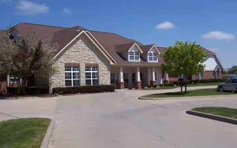 Stone-and-brick senior living facility front entrance with curved driveway and landscaping.