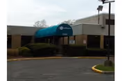 Exterior view of Woodhaven HFA facility entrance with a blue awning and shrubs.