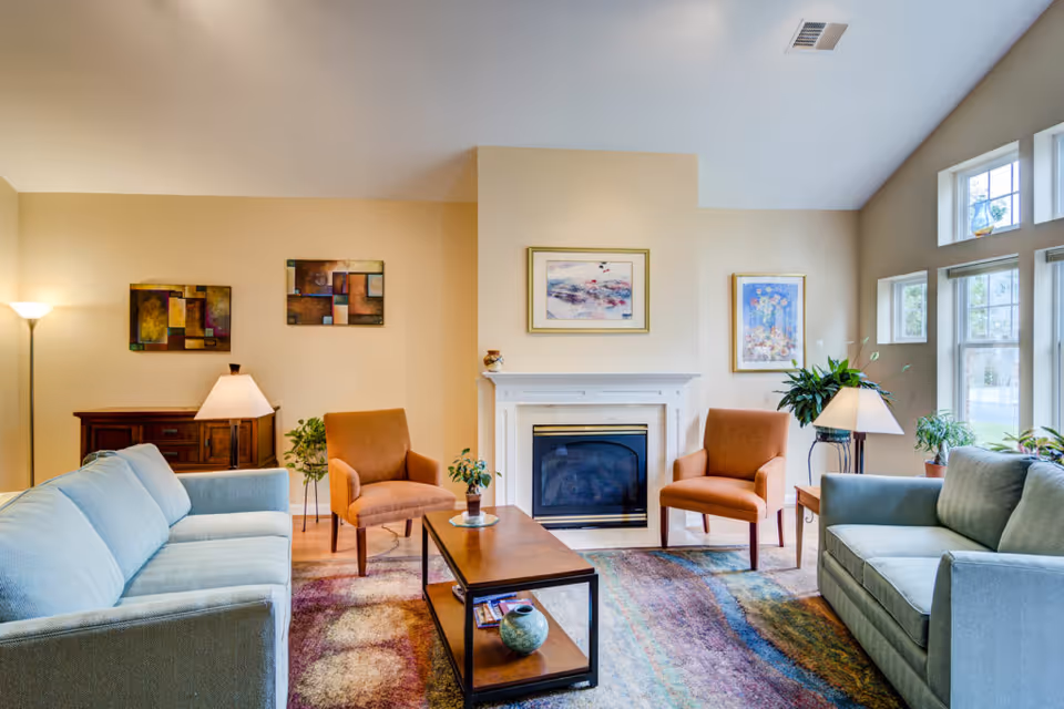 Bright living room with two sofas, two armchairs, a coffee table, a fireplace, and large windows.