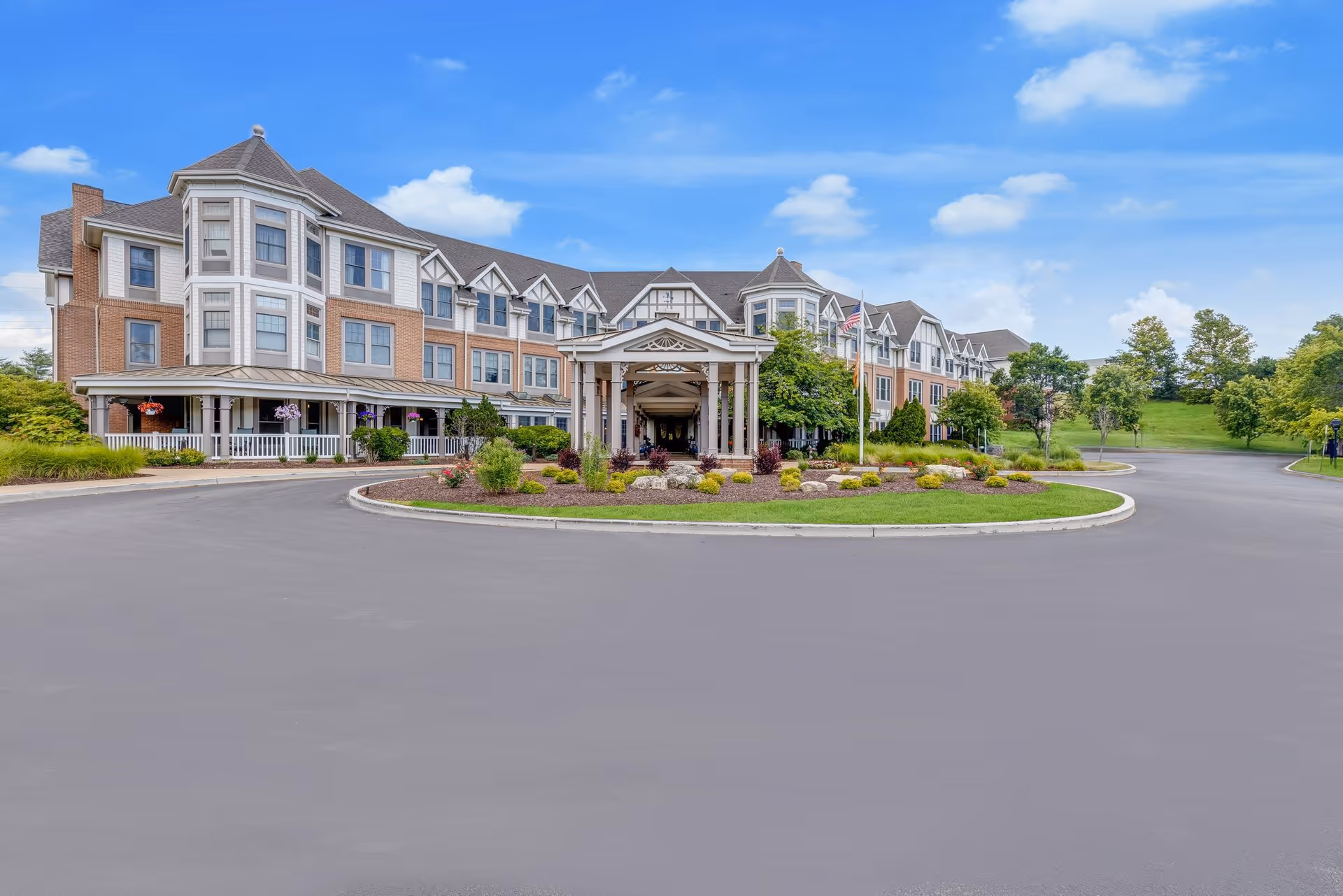 Front exterior of a multi-story senior living building with a covered entrance, circular driveway, and landscaped grounds.