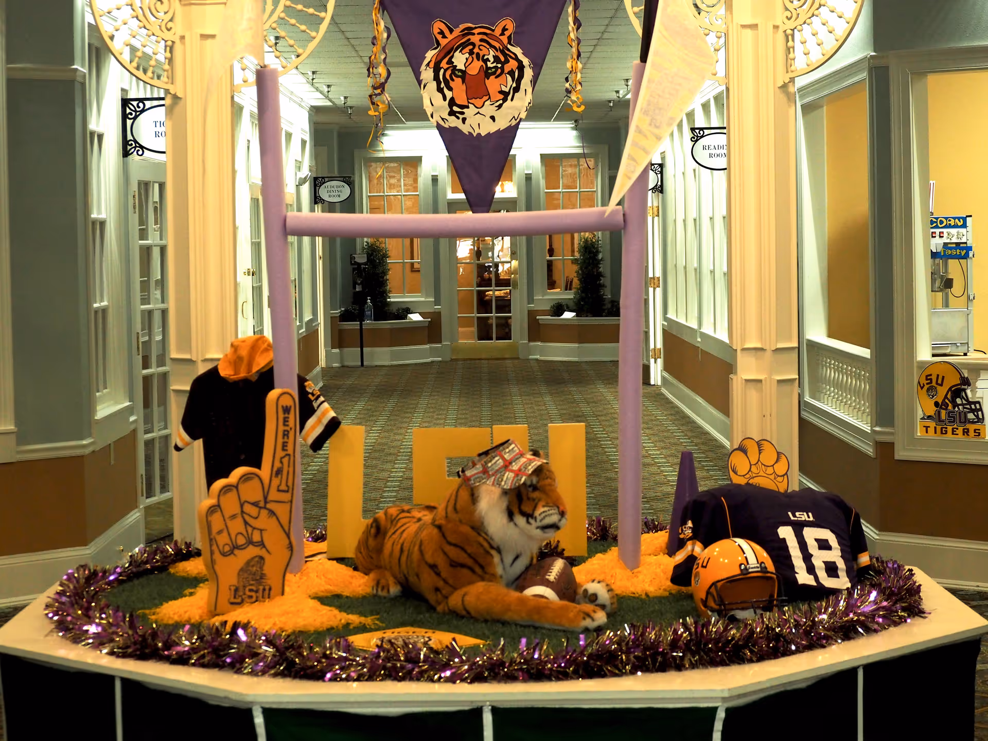 Indoor hallway display with LSU-themed decorations including a stuffed tiger, foam finger, helmet, jerseys and banners.