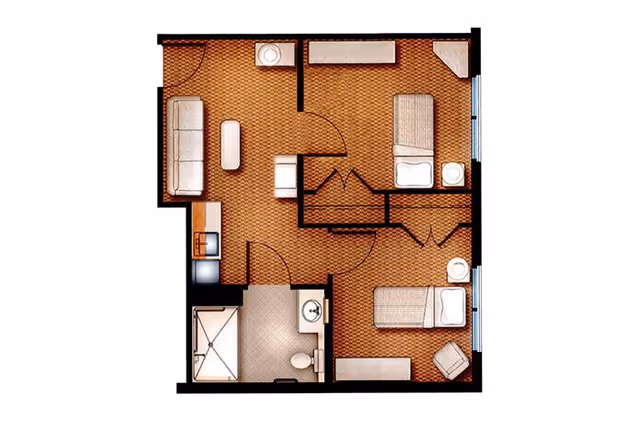 Floor plan of an assisted living unit showing two bedrooms each with a bed and furniture, a living area with a sofa and coffee table, a kitchenette, and a bathroom with a shower, toilet, and sink.