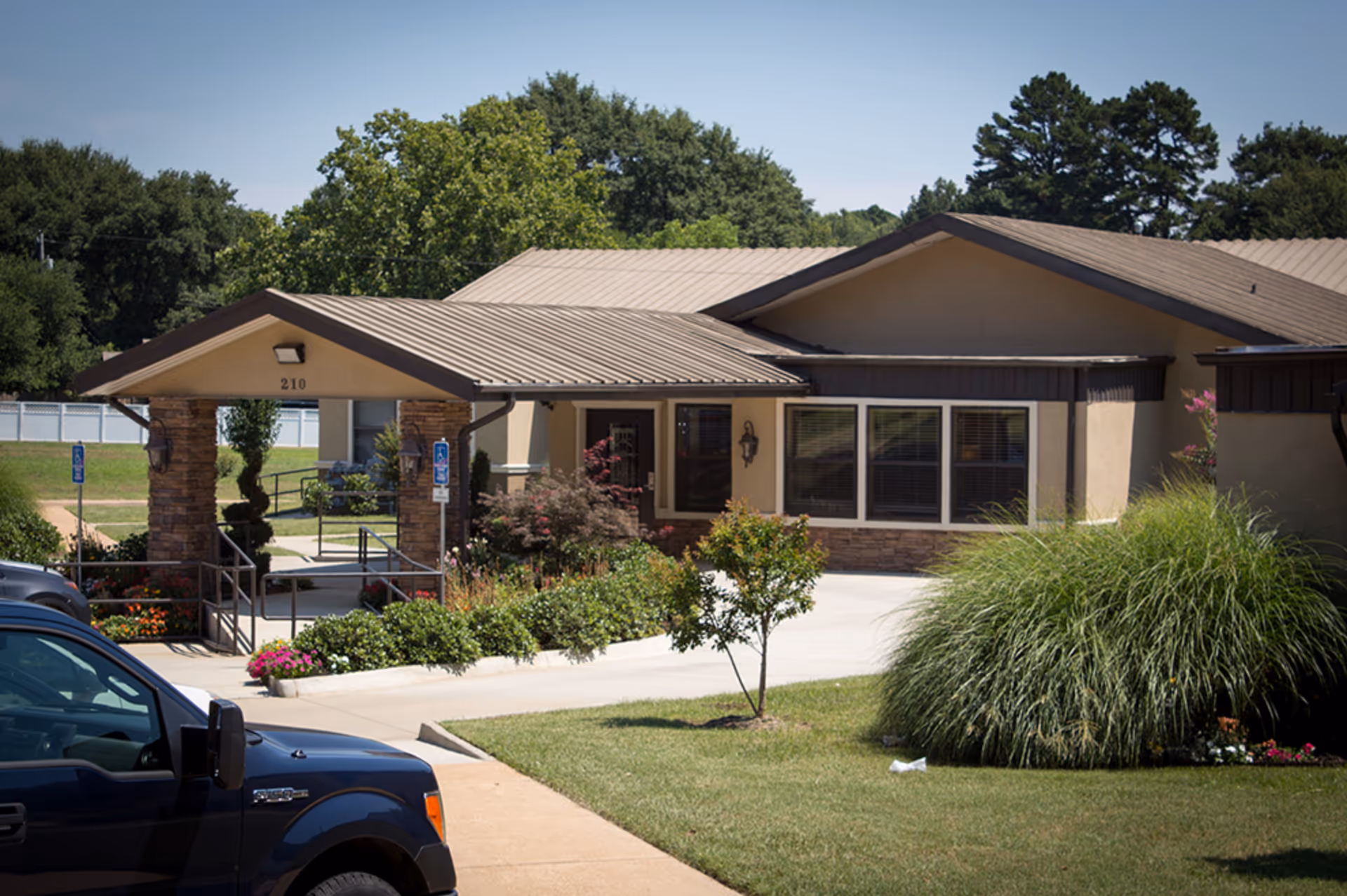 Front entrance of a single-story residential facility with a covered portico, landscaped grounds, and a parked truck.