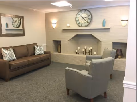 Cozy living room in a senior facility with sofa, chairs, and a decorative fireplace.