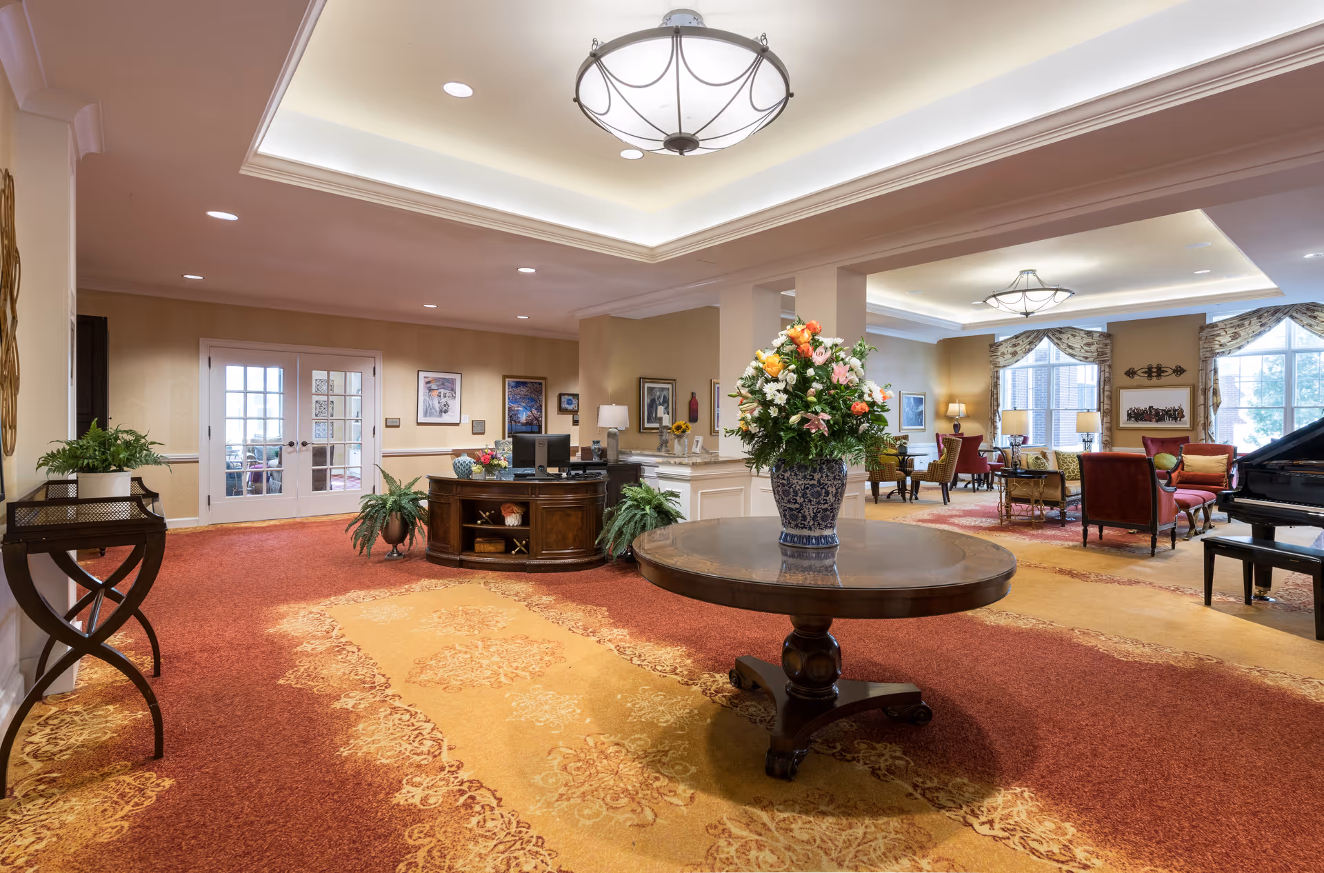 Spacious reception lobby with a round table topped by a large floral arrangement, a front desk, seating areas and a grand piano.