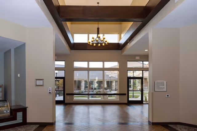 Spacious lobby with high wooden-beamed ceiling, chandelier, and large windows and doors facing an outdoor courtyard.