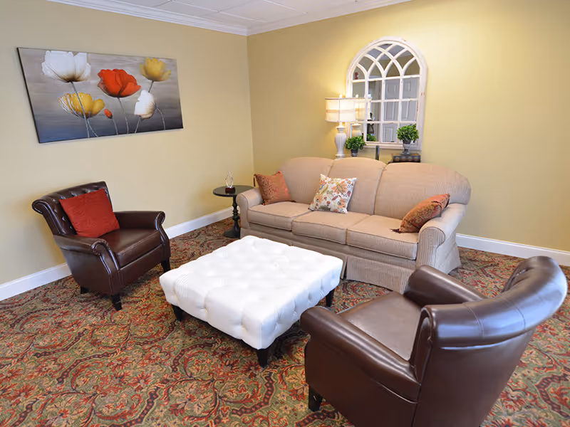 Cozy living room with a beige sofa, two brown leather armchairs, a white tufted ottoman, patterned rug and wall art.