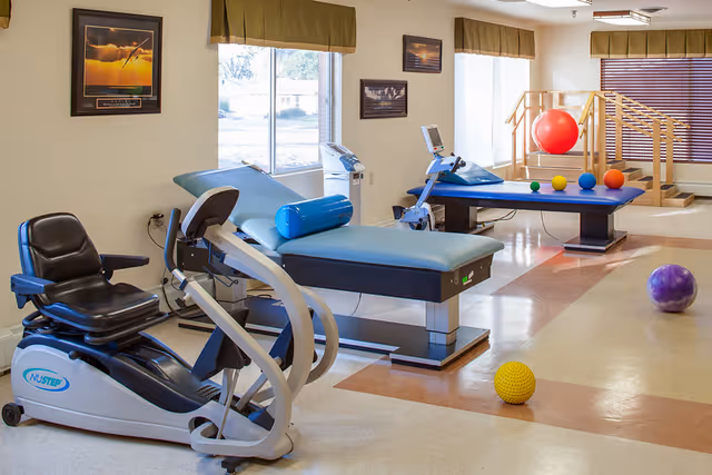 Therapy room interior with exercise tables, a recumbent bike, and various therapy and exercise balls.