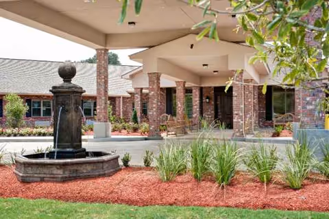 Exterior view of Heritage Manor West entrance with a fountain and manicured landscaping.