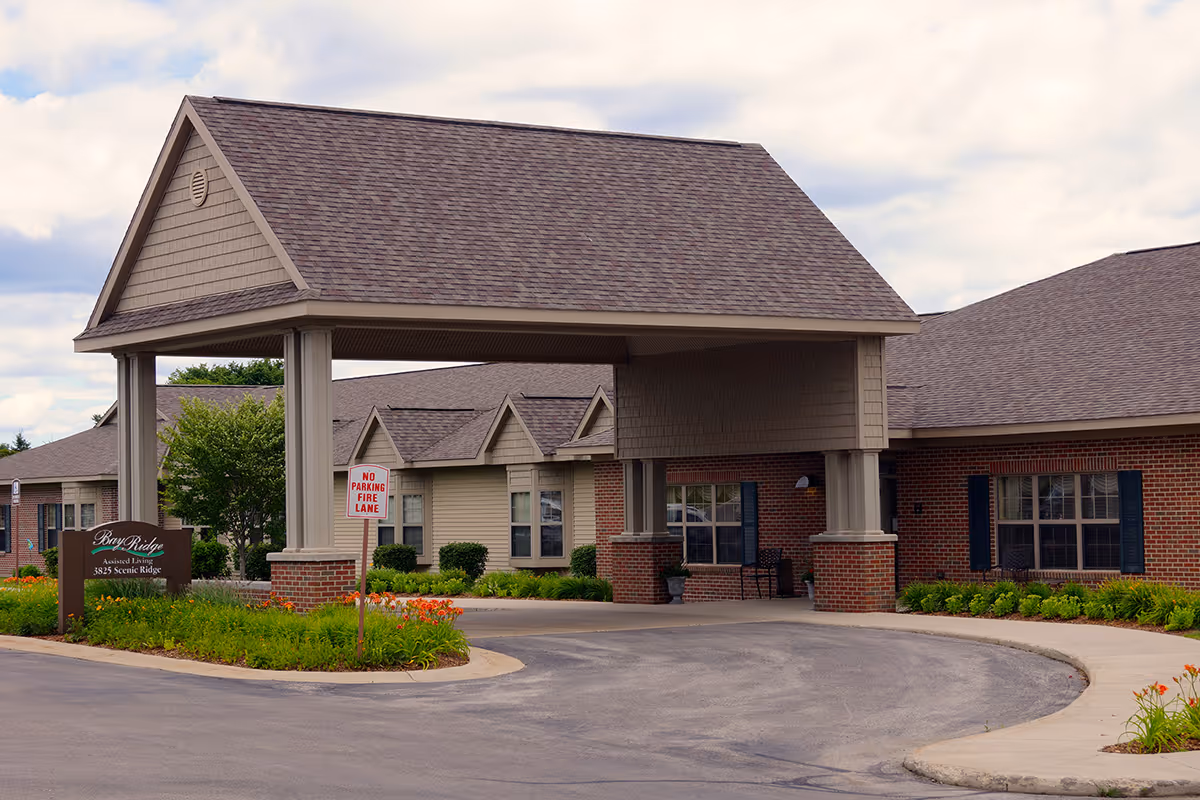 Covered porte-cochere entrance of an assisted living building with a circular driveway and landscaped flowerbeds.