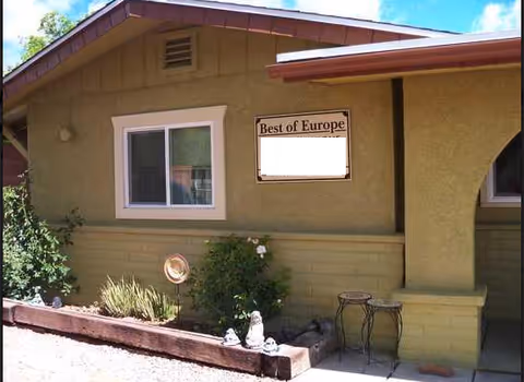 Exterior view of a beige facility with 'Best of Europe' sign, window, and small garden.