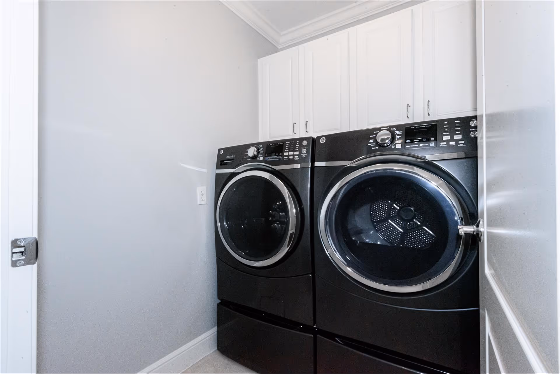 A small laundry room with matching black front-loading washer and dryer beneath white cabinets.