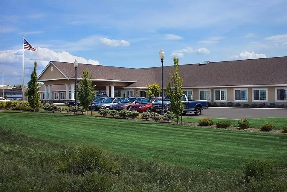 Single-story senior care facility with a parking lot, flagpole, and landscaped lawn.