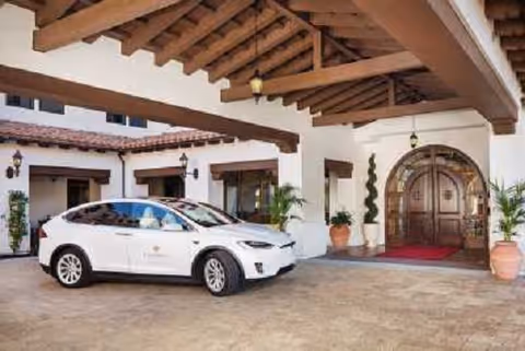 White car parked under a wooden porte-cochere at Crestavilla’s Mediterranean-style building entrance.