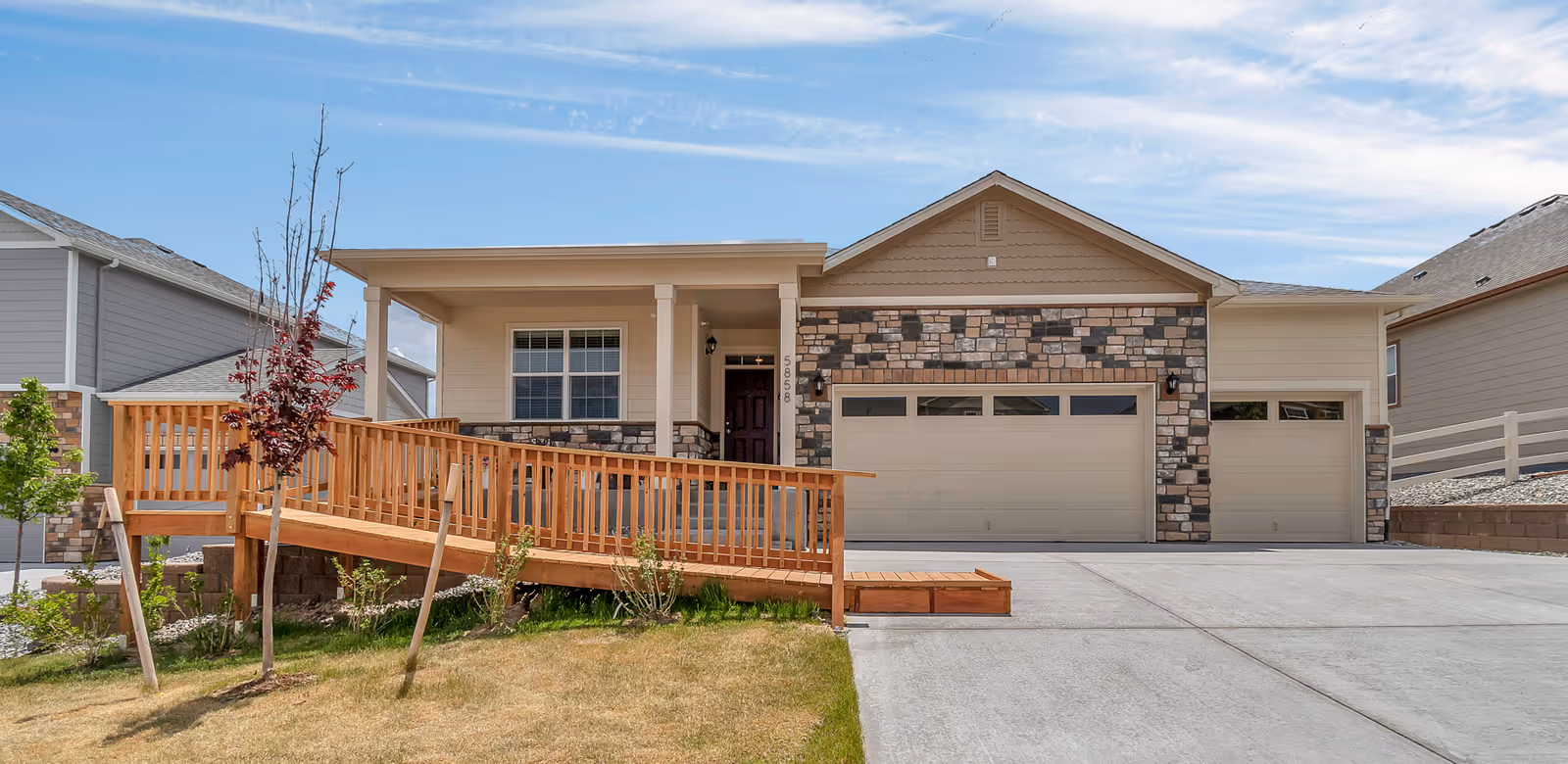 Single-story suburban house front with a wooden wheelchair ramp leading to a covered porch and a three-car garage with stone accents.