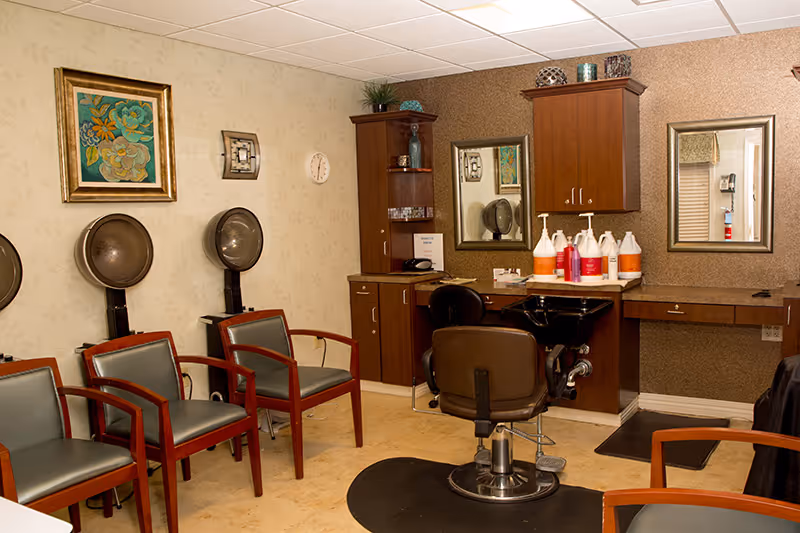 Interior salon with a styling chair and shampoo sink, hooded hair dryers and several waiting chairs.
