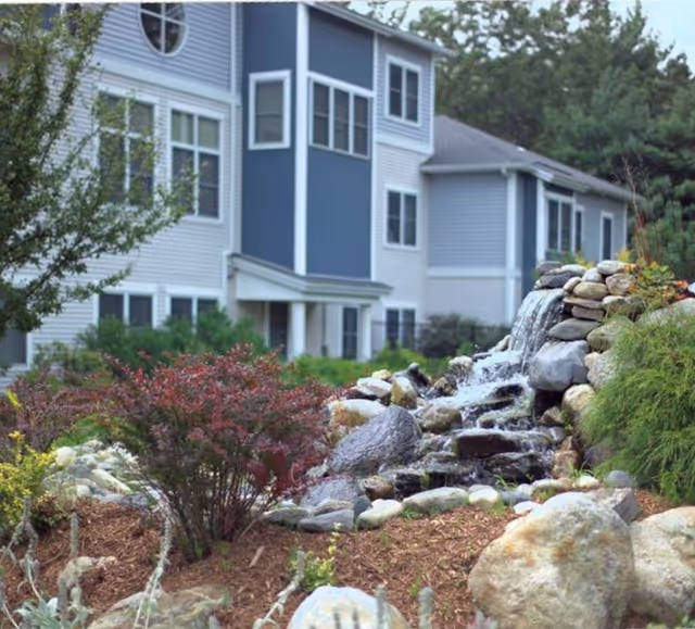 Landscaped outdoor area with a rock waterfall and plants in front of a multi-story residential building.