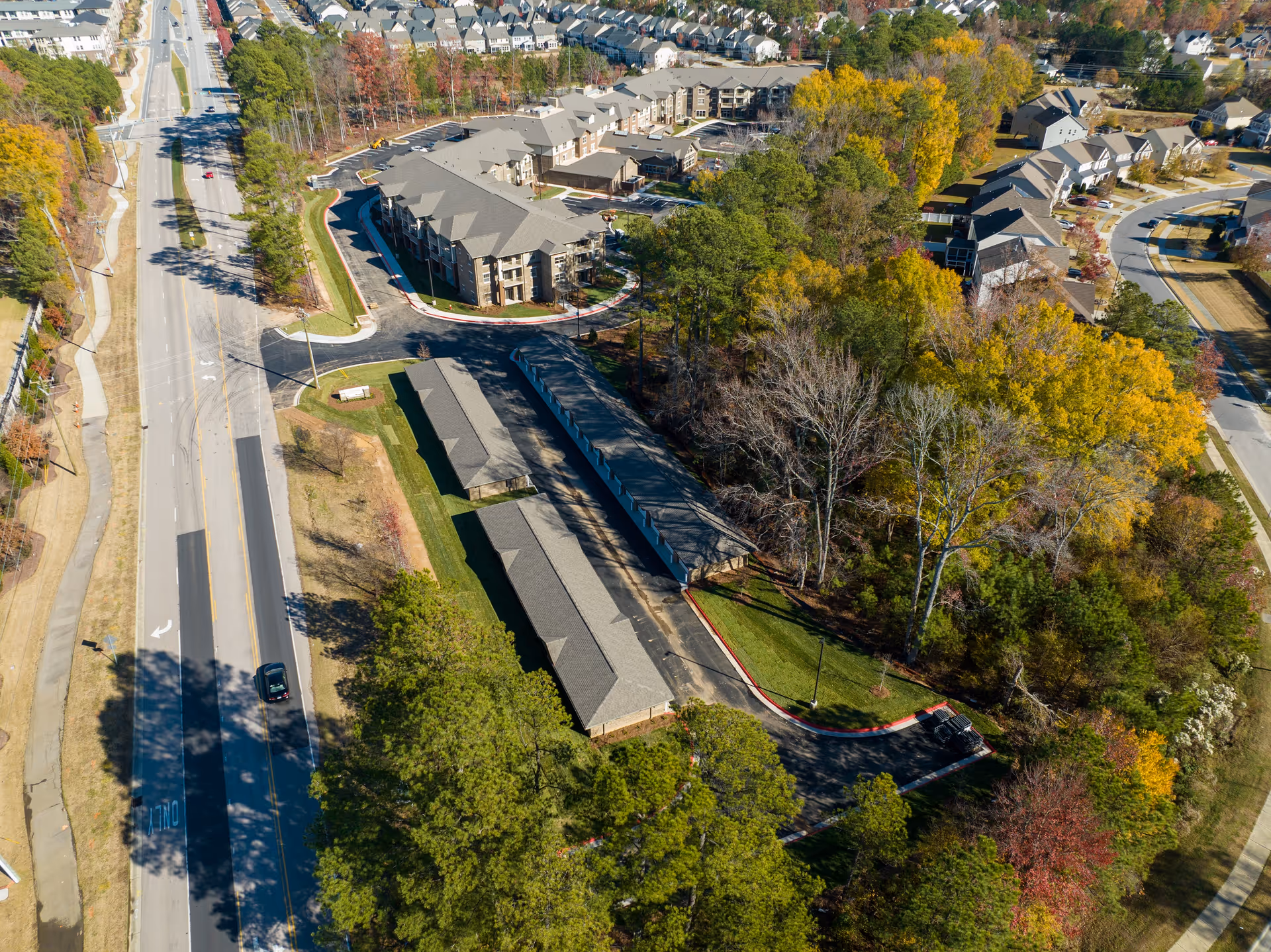 Aerial view of Brier Pointe Retirement Community showing multiple residential buildings surrounded by trees with autumn foliage, adjacent to a main road with sidewalks and a few vehicles.