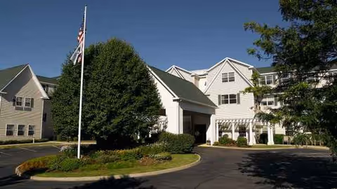 Front view of a multi-story senior living facility with a circular driveway and flagpole.