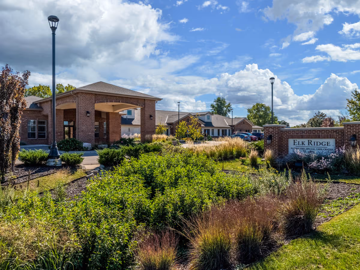 Brick assisted-living building entrance with landscaped grounds and an 'Elk Ridge' sign.