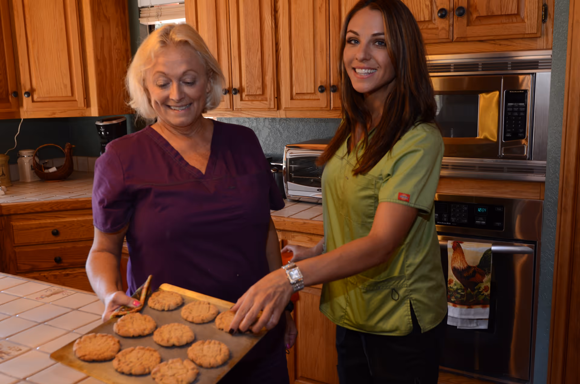Two women in a kitchen smiling as they hold a baking sheet of freshly baked cookies.