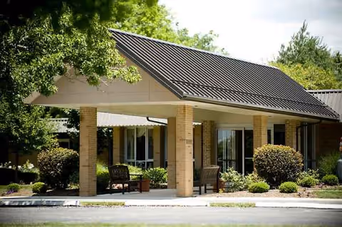 Timbercrest Senior Living exterior with a covered entrance, brick columns, and greenery.