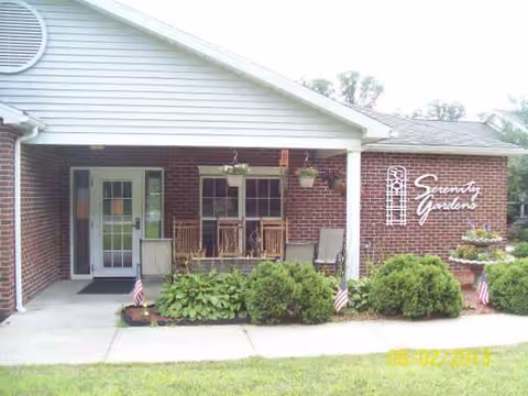 Front view of Serenity Gardens facility with brick exterior, porch seating, and shrubs.
