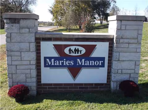 Stone entrance pillars frame a sign reading Maries Manor with trees behind.
