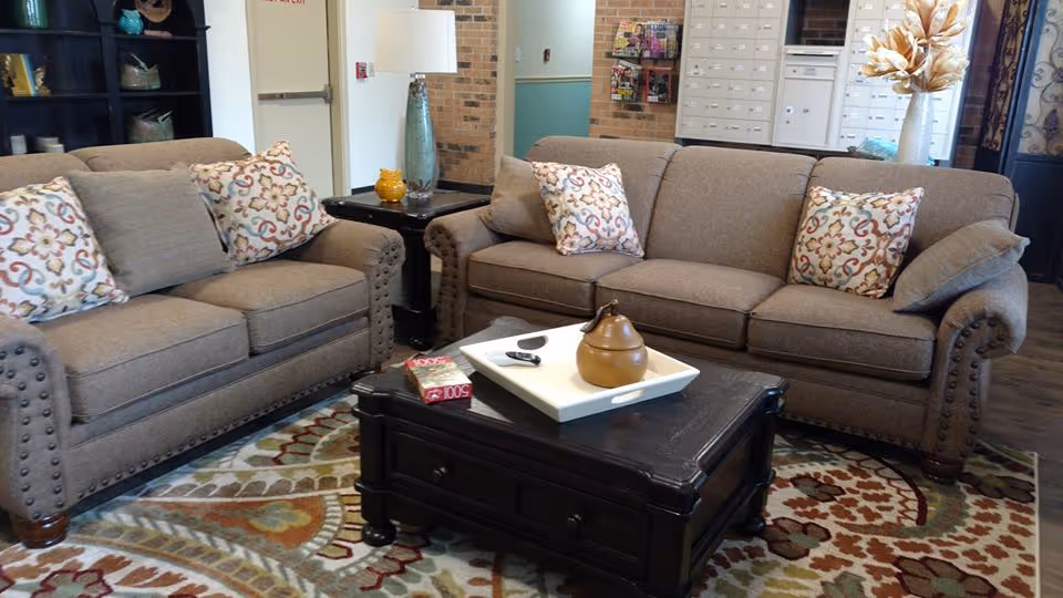 Two upholstered sofas with patterned throw pillows facing a dark wood coffee table on a patterned rug in a cozy lounge area.