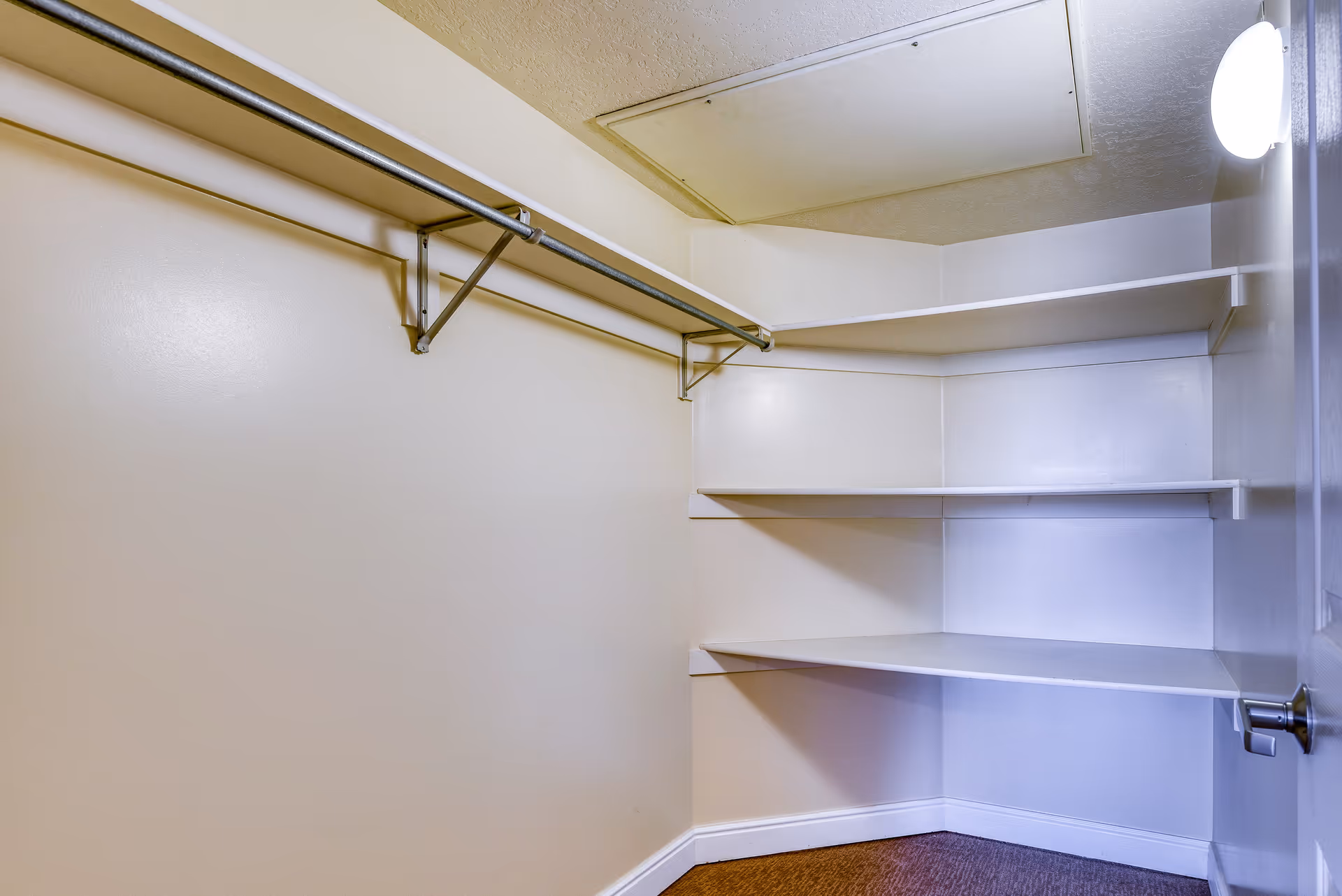 Empty walk-in closet with corner shelves, a hanging rod, and a ceiling access panel.